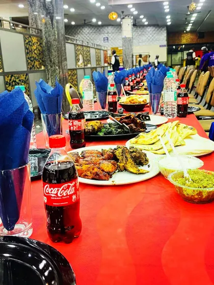 A close-up of a vibrant table setting. The red tablecloth, blue napkins, and colorful array of food like kebabs and naan create a festive and inviting look.