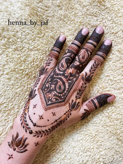 A full view of a bridal henna design with a central geometric shape filled with paisley motifs. The fingers are fully colored, and a leafy vine border completes the look.