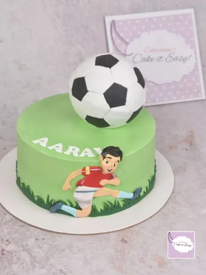 A simple football-themed cake with a 3D ball and a figurine of a player in action.