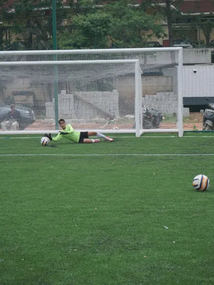 A goalkeeper executes a perfect low diving save, securing the ball on the turf. This drill focuses on proper technique for handling shots aimed at the bottom corners of the goal.