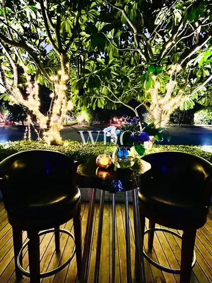 An intimate seating for two on a wooden deck, overlooking a pool and trees wrapped in fairy lights, creating a romantic and magical spot.