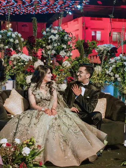 The couple sharing a sweet, candid moment on the Sangeet stage, surrounded by a sea of flowers. Their smiles say it all.