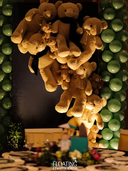 A whimsical installation of teddy bears appears to be climbing a wall next to a column of green balloons. This playful and eye-catching decor element was a favorite among both children and adults at the party.