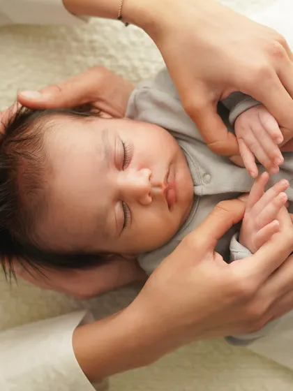 Parents' hands frame their sleeping baby's face, a gesture of love and protection. It's a quiet, intimate moment frozen in time.