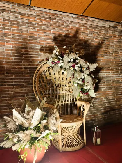 A peacock chair adorned with a large arrangement of dried and fresh flowers. This was a special seating area we created for the bride, combining boho style with a touch of regal elegance.