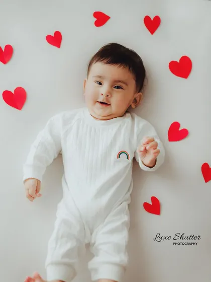 A simple and lovely milestone photo for a five-month-old, lying on a white background surrounded by red paper hearts.