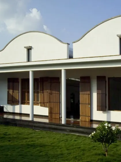 The Synergy Textiles Factory was designed as a protective shell against the harsh Tamil Nadu climate. The facade features a long verandah with deep overhangs and operable wooden shutters, allowing for natural ventilation while shielding the interiors from the sun.