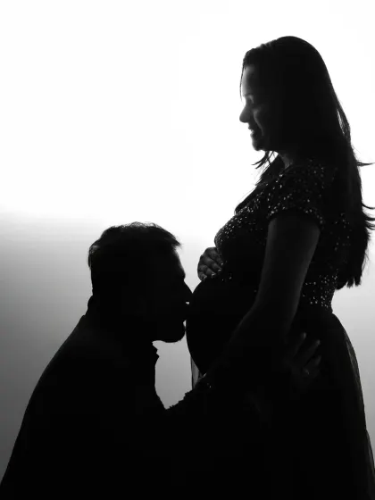 A dramatic black and white silhouette of a partner kissing the baby bump. This artistic studio lighting technique creates a powerful and intimate image that focuses on form and emotion.