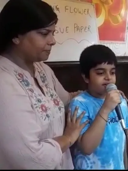 A teacher provides gentle encouragement as a young boy sings during a camp session. This one on one support helps children overcome stage fright and feel comfortable performing.