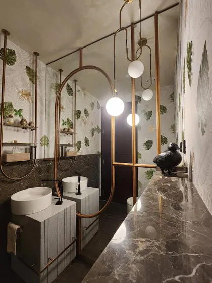 A closer look at the powder room's design, showcasing the interplay of materials. The cool marble of the vanity contrasts with the warm brass framing and the organic leaf-patterned wallpaper, creating a space that is visually rich and intriguing.