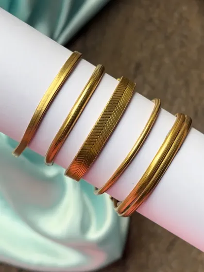 A close-up of our gold-plated stackable bracelets, including a flat herringbone chain and simple round bangles.