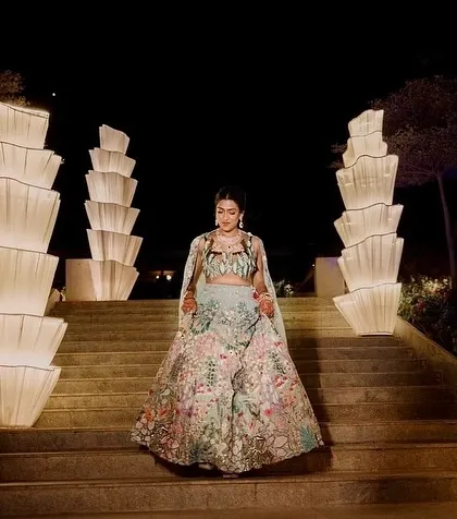 The bride makes her entrance for the Sangeet, walking down a staircase lined with illuminated fabric sculptures.