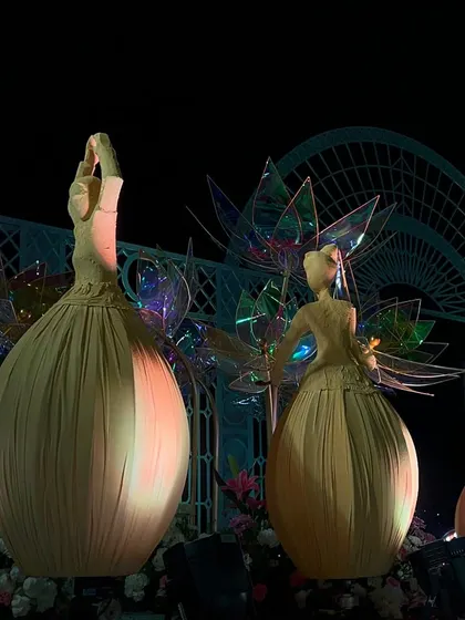 A close-up of the dancing doll sculptures, each one lit from within, set against a backdrop of iridescent lotus flowers.