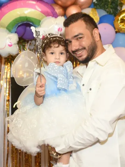 A proud dad holding his little girl, who is dressed up for her birthday party. A sweet father-daughter moment.