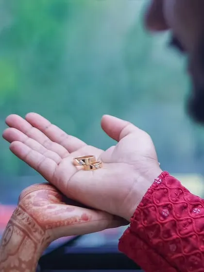 A close-up on the groom's hand holding the wedding rings, with the bride looking on. This photo captures the anticipation and emotion of the moment of exchange.