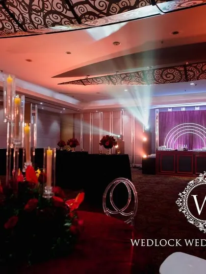 A bold and luxurious reception with a red and black color scheme. The decor includes rich red roses, modern crystal candelabras, and a stylish bar with a neon arch backdrop.