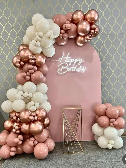 A chic and modern birthday backdrop with a pink arched panel. The balloon garland in rose gold, pink, and white creates a soft and elegant look.