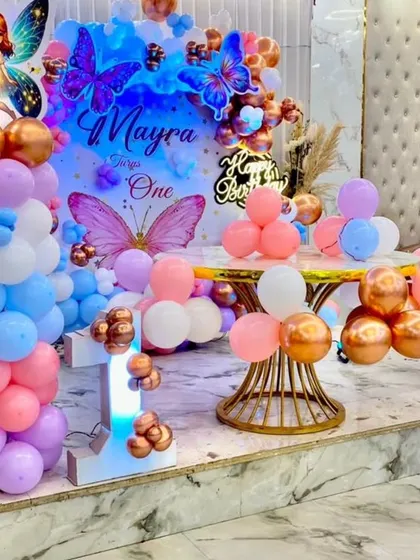 A butterfly-themed first birthday stage for Mayra. The pastel and chrome balloon arrangement on the stage platform creates a dreamy and elegant look.