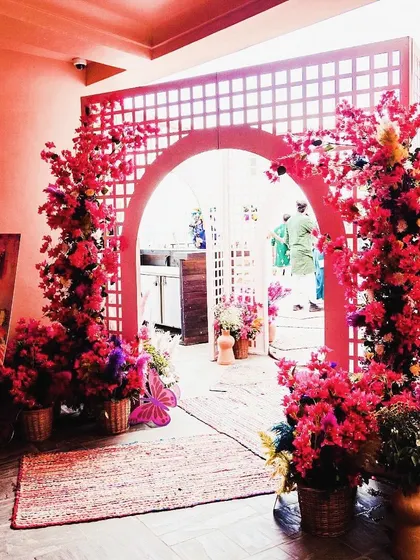 An entrance for a colorful Mehendi, featuring a latticed archway adorned with bright pink floral arrangements, setting a festive tone from the very beginning.