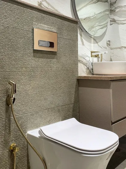 A close-up of the textured stone wall behind the toilet, paired with elegant brushed gold sanitary fixtures from Queo. This combination of materials creates a sophisticated and high-end look.