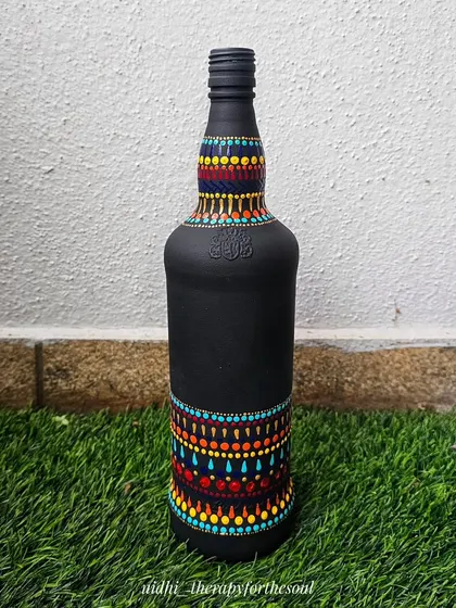A bottle painted with a matte black base and decorated with colorful dot-art patterns on the top and bottom. This style is inspired by aboriginal art and creates a striking look.