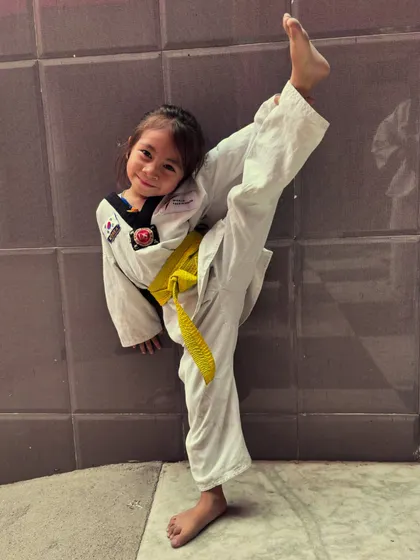 This young girl with a yellow belt shows off her high kick and a big smile. This is what girl power and dedication look like.