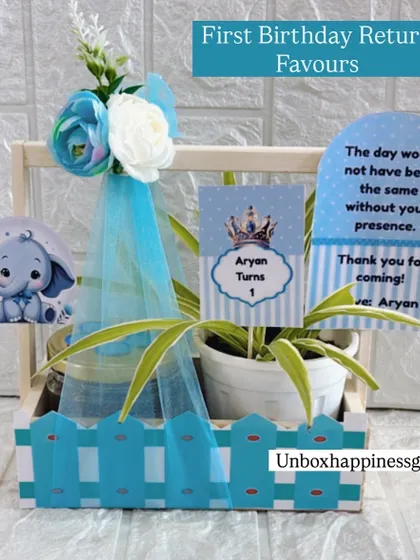 A charming blue return gift basket for Aryan's first birthday. Themed with a cute elephant and crown, it includes a plant and treats, along with a personalized thank you note.