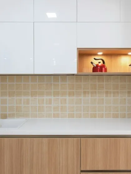 This modern kitchen features a clean, minimalist design with white and wood-finish cabinets, a textured beige backsplash, and a cozy illuminated niche for display.