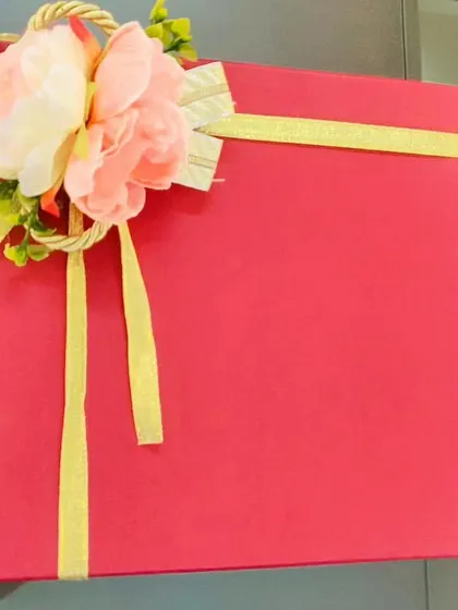 A simple yet elegant red gift box, tied with a golden ribbon and a floral embellishment. This is the perfect canvas for a fully customized gift hamper inside.