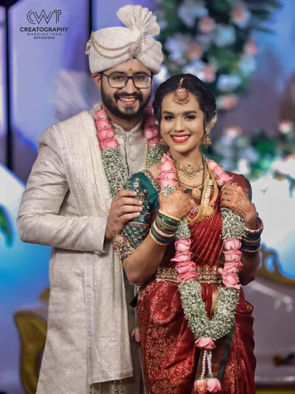 A lovely portrait of a smiling couple, showcasing the bride's beautiful red saree and the groom's elegant sherwani.