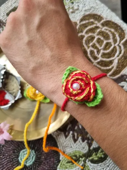 This detailed rose rakhi looks stunning when worn. The layered petals and pearl center make it a truly special piece.