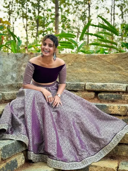 A beautiful shot of a client looking happy and confident in a purple off-shoulder crop top and brocade skirt. This is a perfect outfit for a Sangeet or a friend's wedding reception.