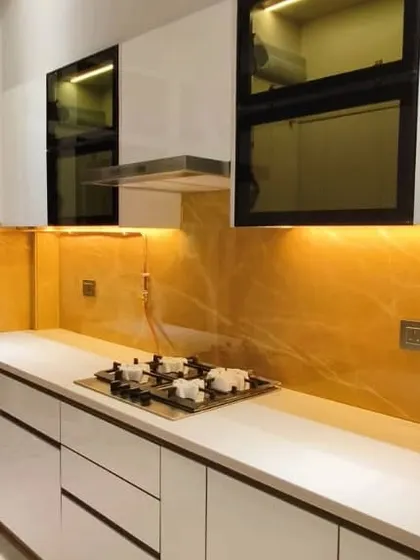 Luxury at its best. This stunning kitchen features white high-gloss cabinets, a vibrant yellow onyx backsplash with backlighting, and a clean, white countertop. The design is both bold and incredibly elegant.