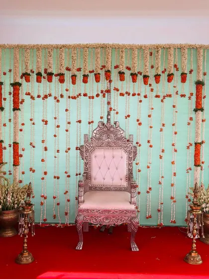A simple yet beautiful backdrop with hanging strings of jasmine and marigold flowers. The light green curtain and red carpet create a classic and festive color combination.