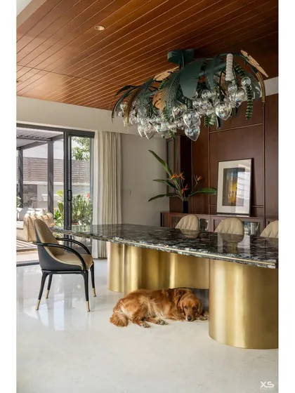 The dining area in the villa continues the theme of refined elegance. A massive marble-topped table with a brass base sits under a custom palm-leaf chandelier, while our furry friend Bruno finds the coolest spot in the house.