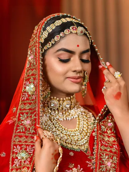A soft, elegant pose capturing the essence of Queen Padmavati. The delicate hand gesture adjusting the embroidered veil showcases the detailed craftsmanship of the red bridal lehenga.
