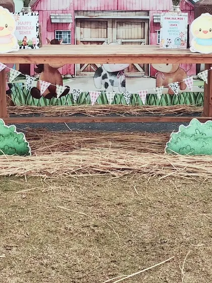 The main cake table setup for the farm party. A rustic wooden table is set in front of the barn backdrop, with hay bales and animal cutouts creating a complete barnyard scene.