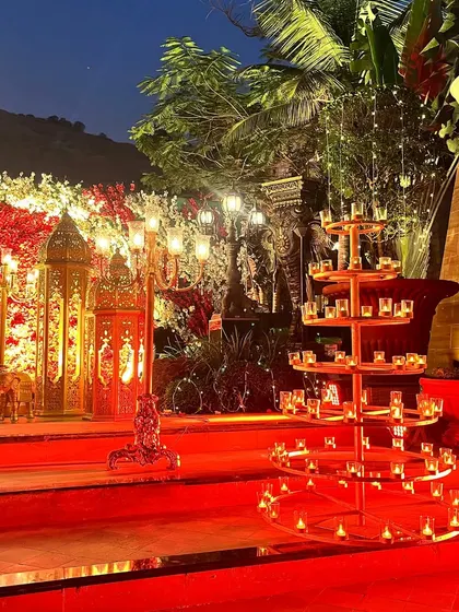 The combination of traditional candelabras, tiered diya stands, and intricate golden gates creates a rich, layered look for this red and gold themed wedding entrance.