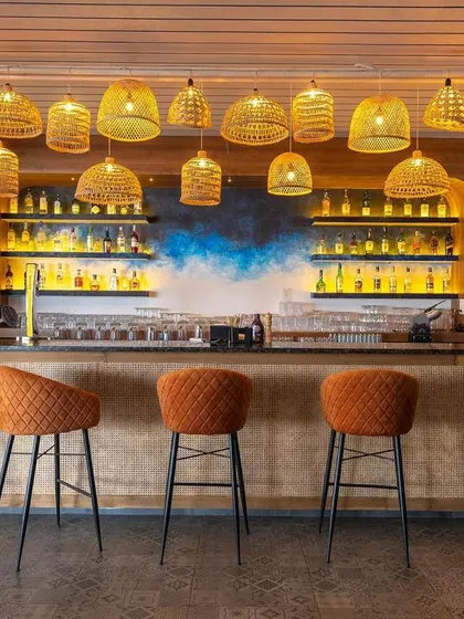 The front view of the bar at "Sloshed," where the warm glow from the cane lights illuminates the space. The design is approachable and stylish, blending natural textures with modern comfort.