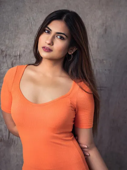 A simple, natural light portrait against a textured wall. The bright orange top adds a pop of color, making this a great headshot or portfolio image.
