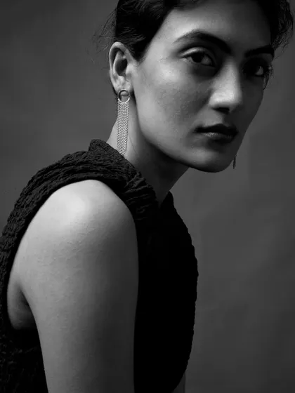 A quiet, sculptural portrait in black and white. The lighting is carefully shaped to highlight the texture of the clothing and the elegant lines of her profile.