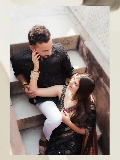 An intimate, high-angle portrait of a couple sharing a moment on a stone staircase. This candid-style shot focuses on their gentle interaction and the beautiful textures of their traditional outfits.