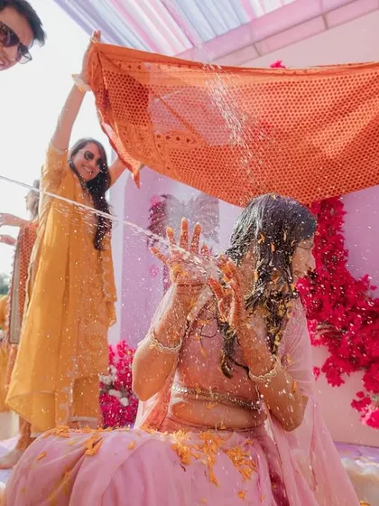 The bride gets a champagne shower during her Haldi, a fun twist on the traditional ceremony, captured in a dynamic action shot.