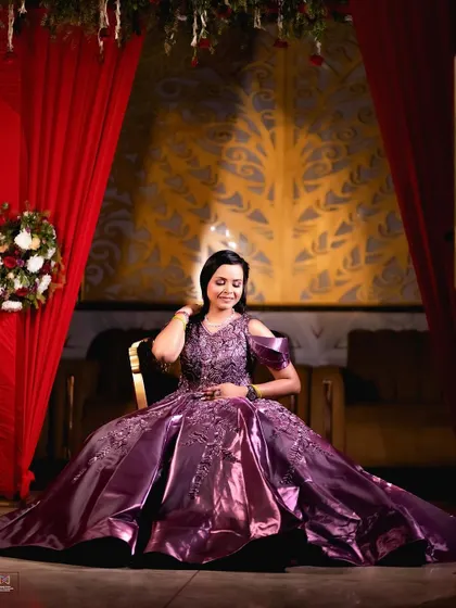 A full-length shot of the bride-to-be seated, showcasing the magnificent spread of her embroidered gown. The dramatic red curtains in the background frame her beautifully.