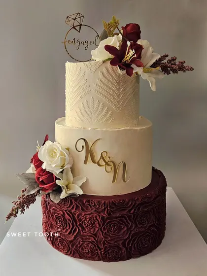 An elegant three-tier engagement cake. This butterscotch cake features a maroon rosette bottom tier, a stenciled top tier, and beautiful floral arrangements.