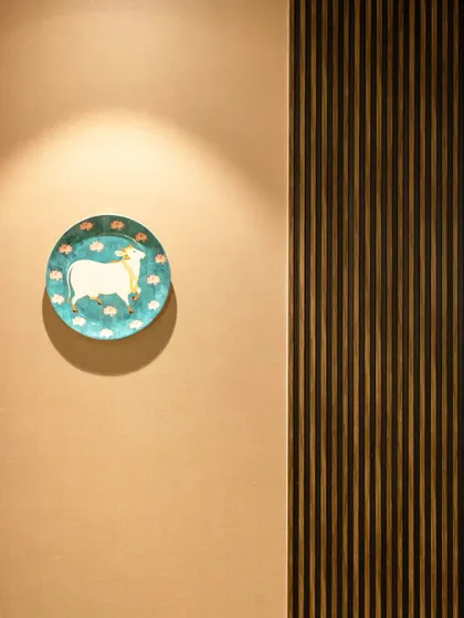 A single, artful plate is highlighted by a spotlight, turning it into a small piece of gallery-worthy art. This is next to vertical wooden fluting, creating a play of textures.