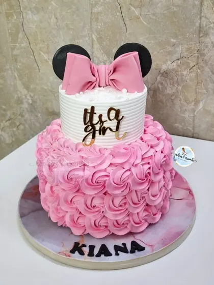 A minimal and beautiful Minnie Mouse themed cake for a baby girl's welcome party. The bottom tier features a pink rosette design, while the top is clean and simple with a fondant bow.