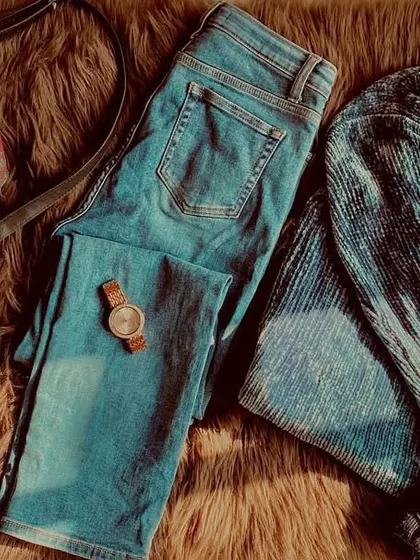 A flat lay of a cozy blue winter outfit. This shows all the components of a great look: a comfy sweater, jeans, and the right accessories like a watch and bag.
