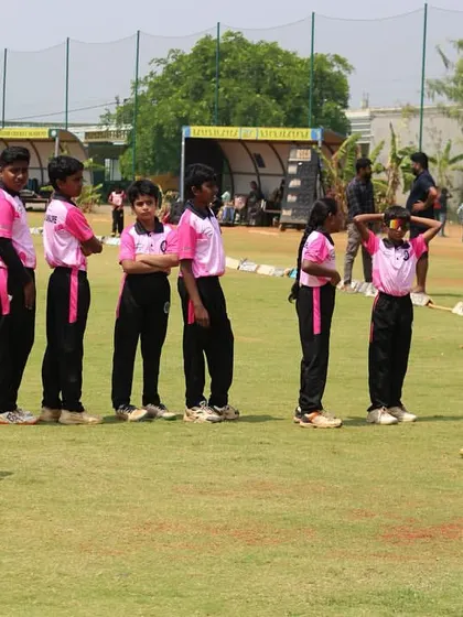 A youth team in their pink jerseys listens to a coach during a strategy talk on the field.