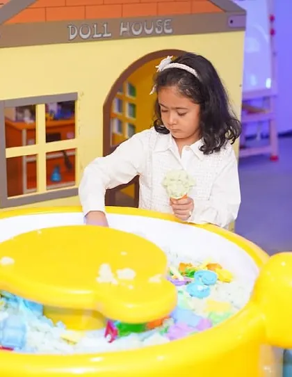 A girl engages in sensory play at our sand table, located right next to the pretend-play dollhouse.